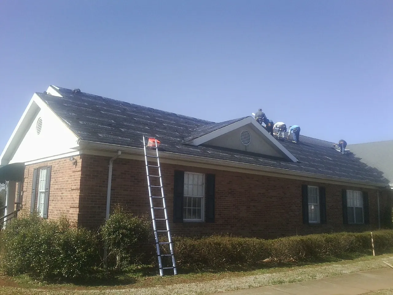 Crew tearing shingles off a brick ranch roof with a ladder set — Metal Roof Repair work by our crew in Thompsontown