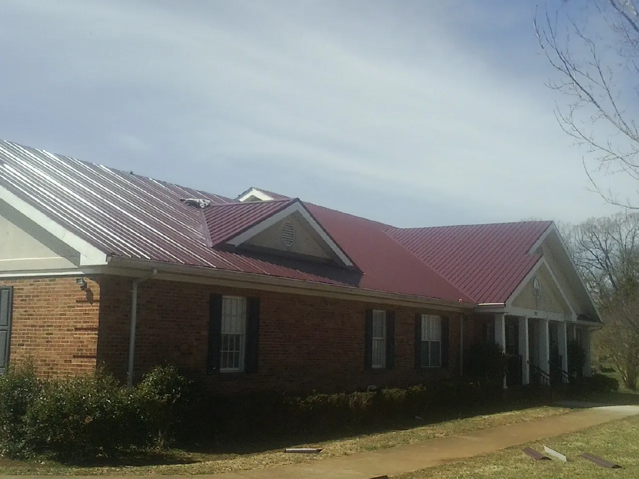 Red metal roof with gabled entries on a long brick building, from a Hail Damage Roof Repair job in Thompsontown