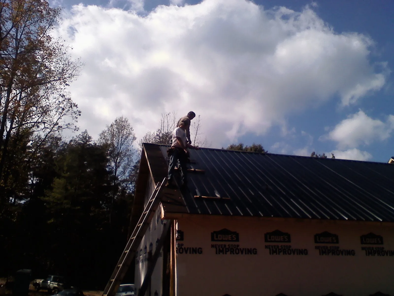 Roofer fastening dark metal panels high against a cloudy sky, from a Roof Inspection job in Thompsontown