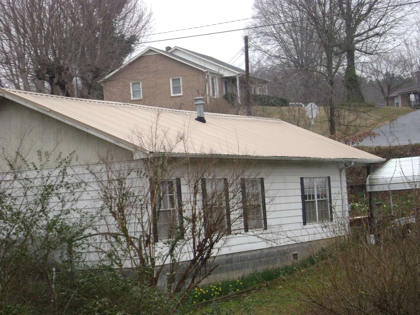 Tan metal roof on a white sided house set into a hillside — Commercial Roofing by Roofing Brothers in Thompsontown